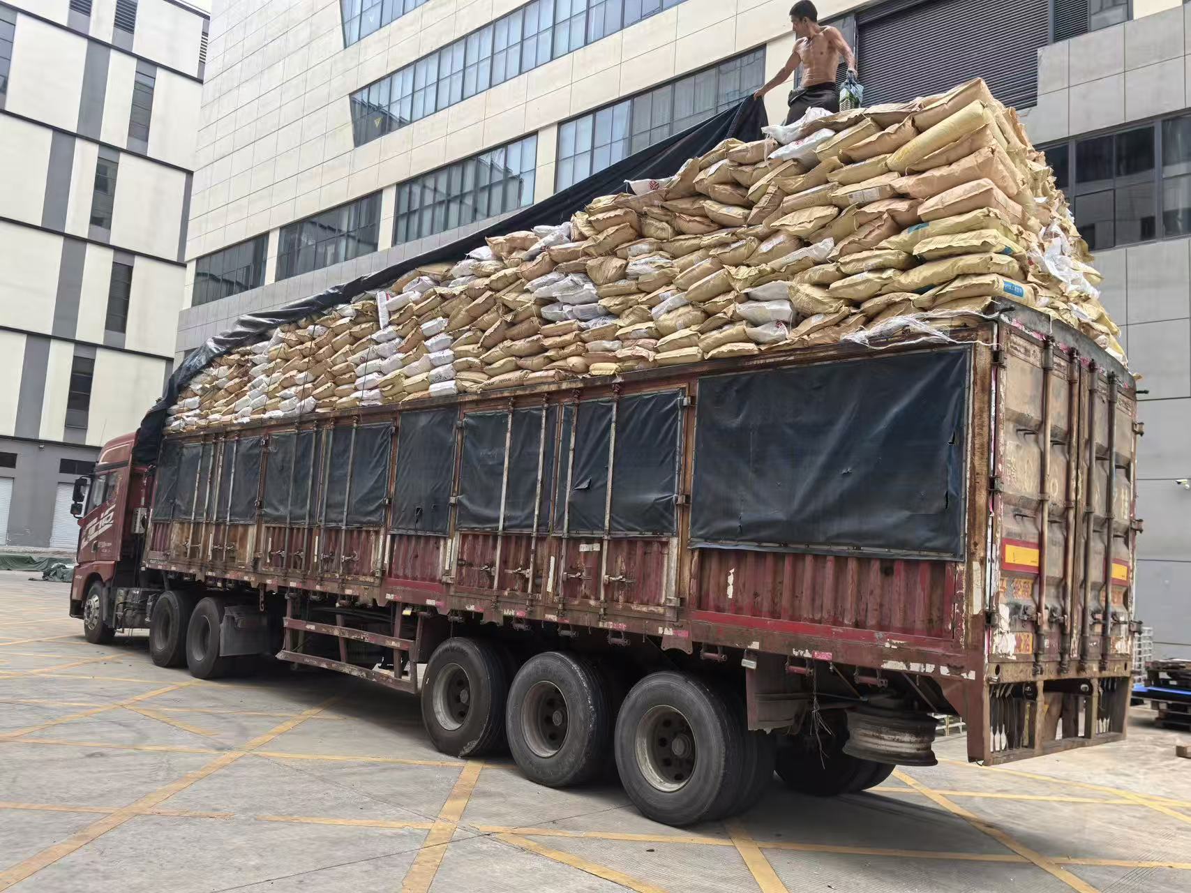 工人在货车顶部整理捆扎装载的原料袋